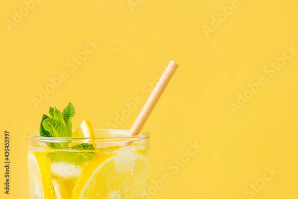 Fototapeta Summer drink with lemon and mint in glass with paper straw on yellow background. Fresh nonalcoholic mojito with exotic fruit and ice. Copy space