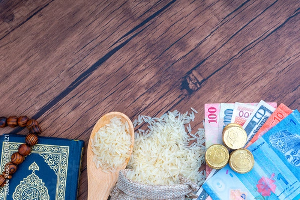 Obraz Holy Al Quran, Coins, Banknotes and Rice on wooden background. Zakat concept. Zakat is a form of alm-giving as a religious obligation