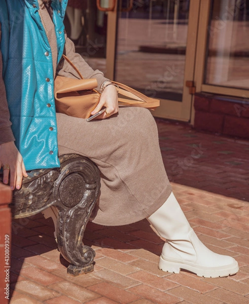 Obraz A girl in white leather boots sits on a bench .