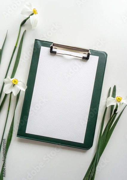Obraz Green clipboard with daffodils on white background, home office workspace flat lay.