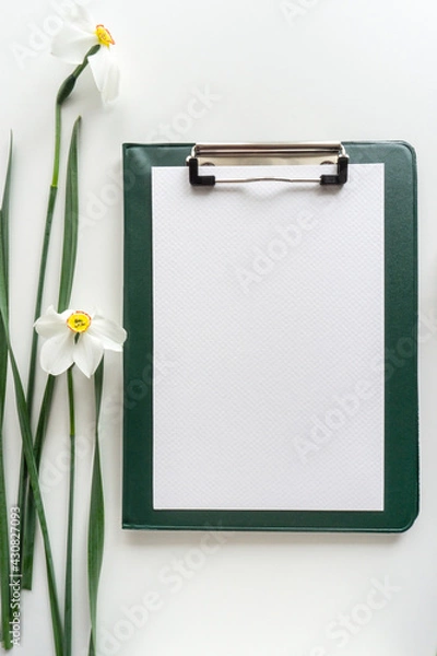 Obraz Green clipboard with daffodils on white background, home office workspace flat lay.