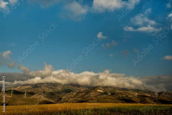 Fototapeta View of the mountains with clouds and wind turbines on the hills.
