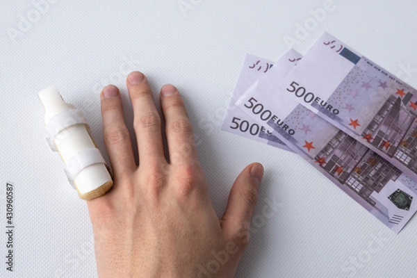 Fototapeta medical splint on a broken finger and money on a white background. Expensive medical services and insurance