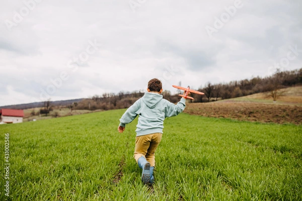 Fototapeta Boy playing with a red plane in a field with green grass, running.