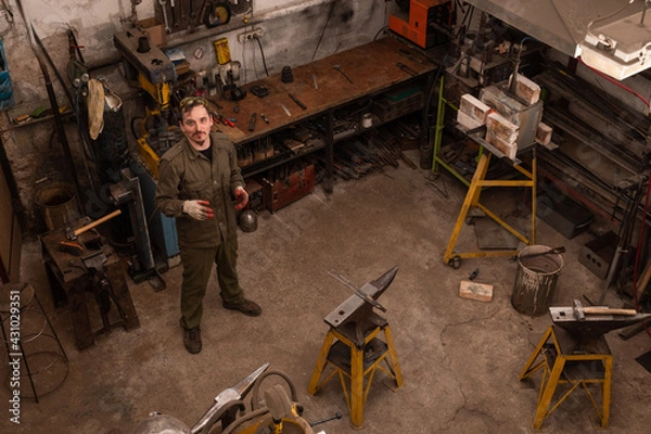 Fototapeta Traditional metalworking process in a forge. Blacksmith in the workshop posing, top view.