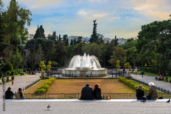 Fototapeta Athens, Attica, Greece. The marble fountain in front of the Zappeion Hall neoclassical building in the National Garden of Athens near Syntagma Square. People relaxing under the sun