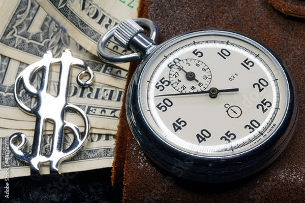 Fototapeta Dollar close-up. Money macro shot. The stopwatch lies on paper banknotes and a leather wallet. Clock, watch, timepiece, timer, clock face, mechanical device, speedometer                            