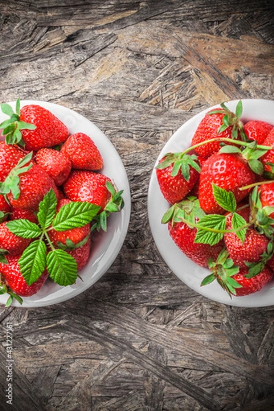 Fototapeta Strawberries fresh overhead ready to eat spring arrangement with green leaves in white ceramic jars on wooden table in studio
