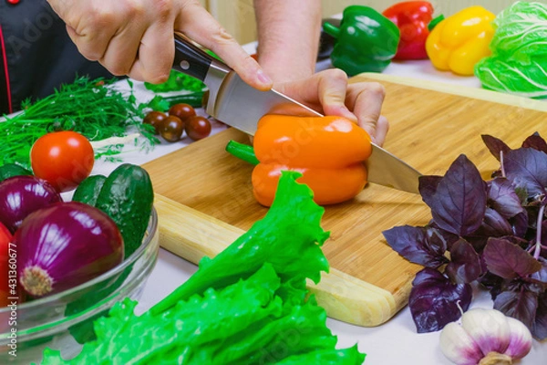 Obraz Chef cuts orange paprika on a cutting Board