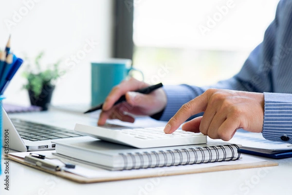 Fototapeta Close up Business man using calculator and laptop for do math finance on wooden desk, tax, accounting, statistics and analytical research concept
