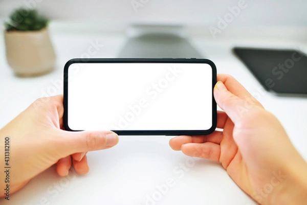 Fototapeta Mockup image of woman's hands holding and using a black mobile phone with blank screen horizontally for watching.