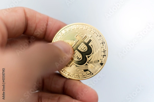 Fototapeta Bitcoin. Hand holding gold coin with BTC symbol. Person investing in virtual assets like cryptocurrency concept background