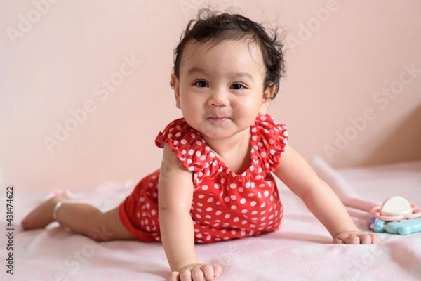 Obraz Little smiling Asian baby, a cute toddler dressed in red practicing crawling on the bed and looking at the camera