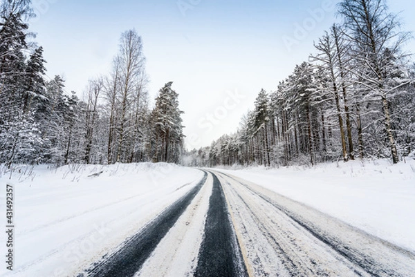 Fototapeta Snowfall on a winter day, snow-covered country road. View from the side of the road. Coniferous forest. Russia, Europe. Beautiful nature.