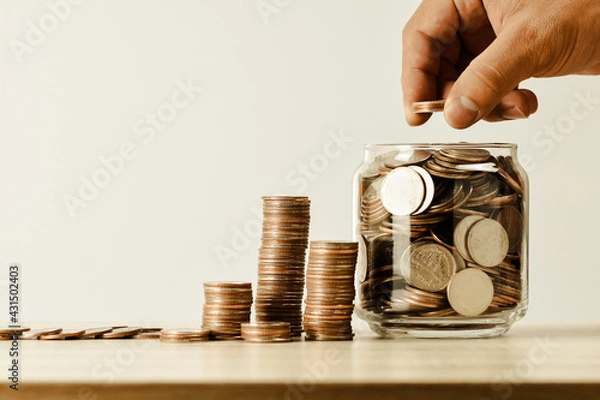 Fototapeta Thai coins are lined up and hand holding money in a jar on the table shown in the form of a graph vintage tone , business and financial, saving concept