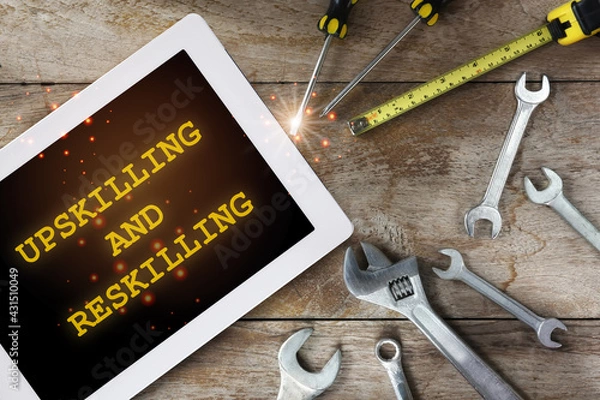 Fototapeta Upskilling and reskilling words on digital computer tablet and tools supplies on wooden background. New skills concept and technology transformation learning model idea