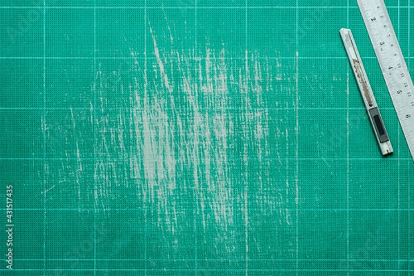 Fototapeta Old grunge green dirty cutting mat, with stainless steel ruler and cutter, grunge texture background,  top view of workspace, copy space for text and graphic.