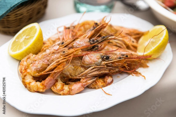 Obraz Baked prawns with lemon halves on a white plate.