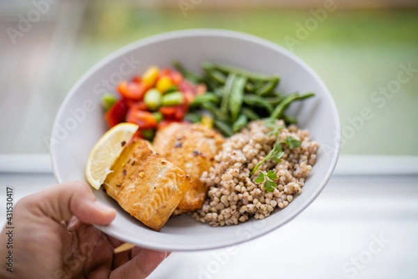 Fototapeta Hand holding salmon and buckwheat dish with green beans