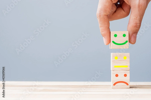 Fototapeta Hand holding smile face symbol on wooden cube blocks. Emotion, Service rating, ranking, customer review, satisfaction and feedback concept