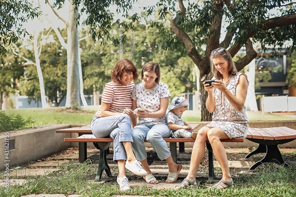 Obraz Three women friends with baby strollers reading text message in park