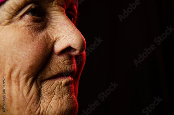 Fototapeta Old grandmother's face close up. Close-up of wrinkled old face. A portrait photo of an old grandmother. An old face in the dark. Aged skin on the face. Seniors concept