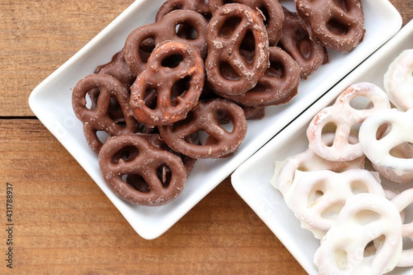 Fototapeta White and dark salted chocolate covered mini pretzels in a bowl on wood table. Homemade assorted mini pretzel chip cookies on plates on wooden background. Top view, copy space
