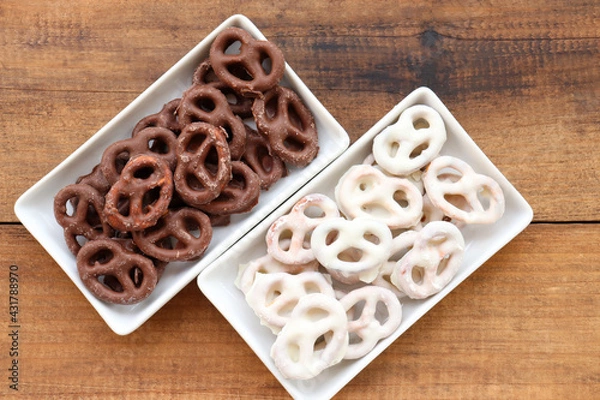 Fototapeta White and dark salted chocolate covered mini pretzels in a bowl on wood table. Homemade assorted mini pretzel chip cookies on plates on wooden background. Top view, copy space
