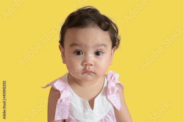 Obraz Portrait of a cute little Asian baby girl, look at camera isolated on yellow background, baby expression concept