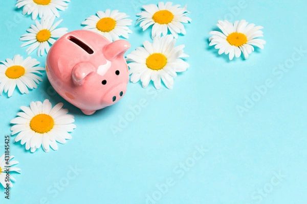 Obraz Pink piggy bank with chamomile flowers on a blue background. Copy space for text. Save up money for the summer.