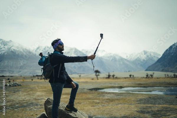 Fototapeta Young and handsome male travel blogger recording a video for vlog with his Go Pro action camera, making vlog for youtube.