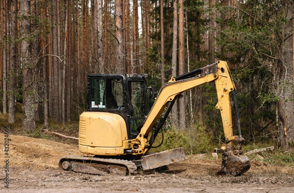 Fototapeta Yellow belt excavator in a pine forest. Hydraulic earthmoving harvester. Rotating operator's cab. Construction industry.