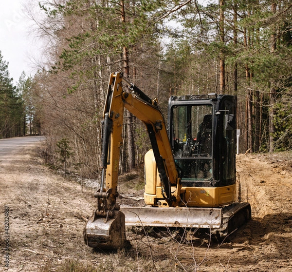 Fototapeta Yellow belt excavator in a pine forest. Hydraulic earthmoving harvester. Rotating operator's cab. Construction industry.