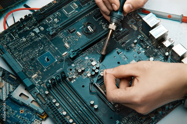 Fototapeta A man holds a tool for repairing electronics, manually assembling a solder circuit board.