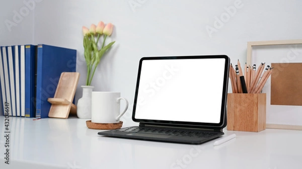 Fototapeta Neat and ordered workspace with computer tablet, coffee cup, books and office supplies on white table.
