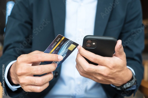 Fototapeta Businessman in suit holding credit card and using touchscreen smartphone for online shopping while making orders in the cafe or office .business, technology, ecommerce and online payment concept