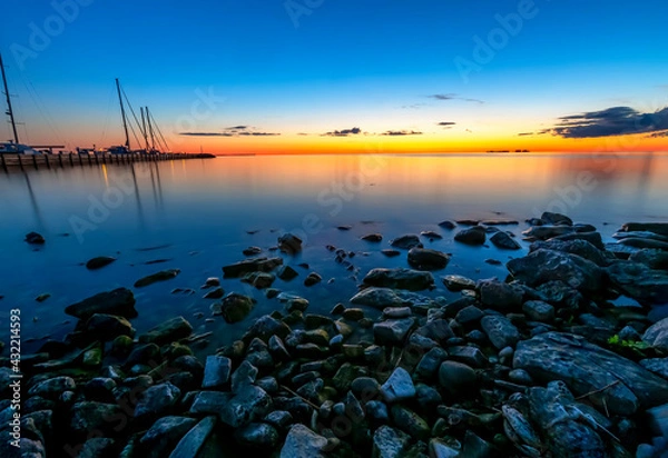 Fototapeta With shoreline rocks and boats in the marina to the left, a beautiful sunset is reflected on the waters of Sister Bay, Wisconsin in Door County, a peninsula extending into Great Lake Michigan.