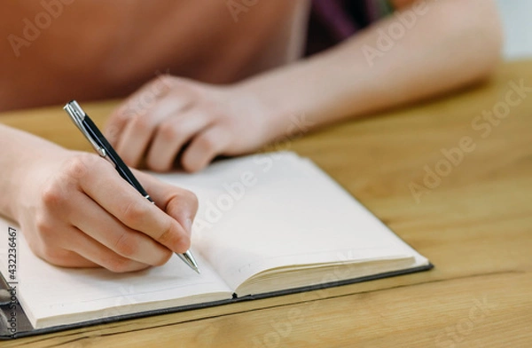 Fototapeta Close-up of a student's hand holding a pen and making notes in a notebook