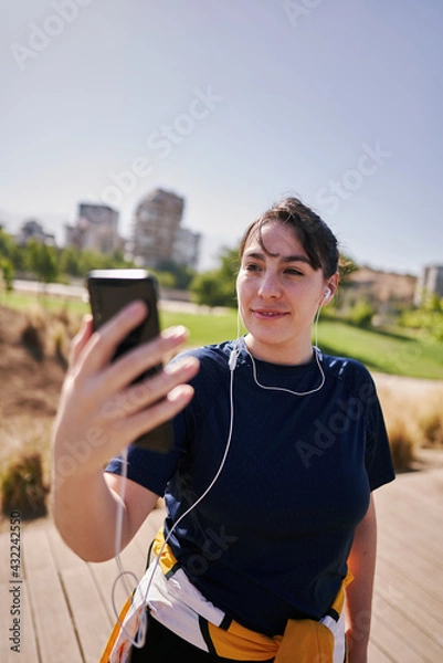 Obraz  A beautiful white woman with brown hair and a sports outfit sends a message by cell phone to one of her friends