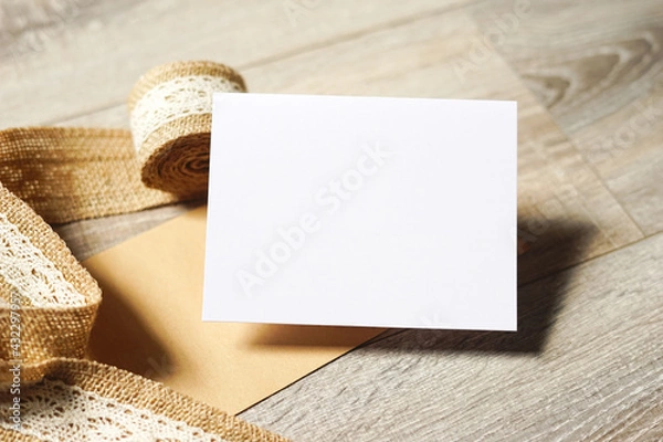 Fototapeta Blank white card on wooden background with a natural paper envelope and burlap ribbon. Empty space for text. Copy space.