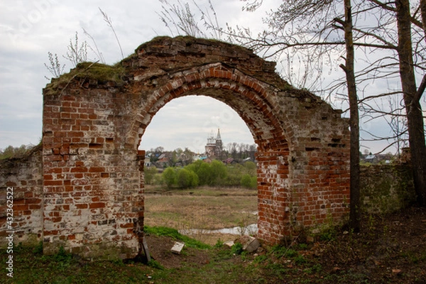 Fototapeta Old red brick wall gate and view to the church, river, countryside in cloudy spring day