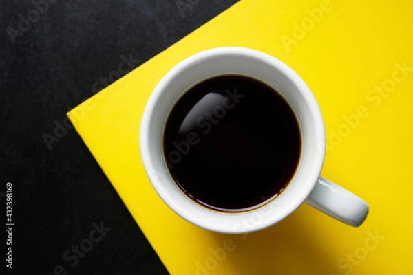 Obraz Top view a cup of black coffee on yellow paper and black table background.   