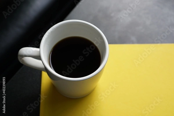 Obraz A cup of black coffee on yellow paper and loft style table and part of sofa background.
