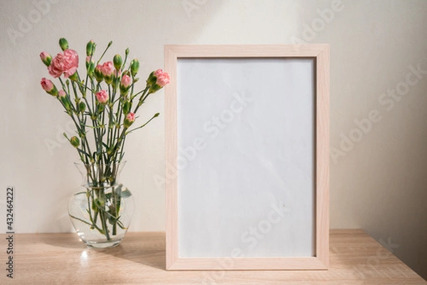 Fototapeta Portrait white picture frame mockup on wooden table. Modern ceramic vase with carnation. White wall background. Scandinavian interior. 