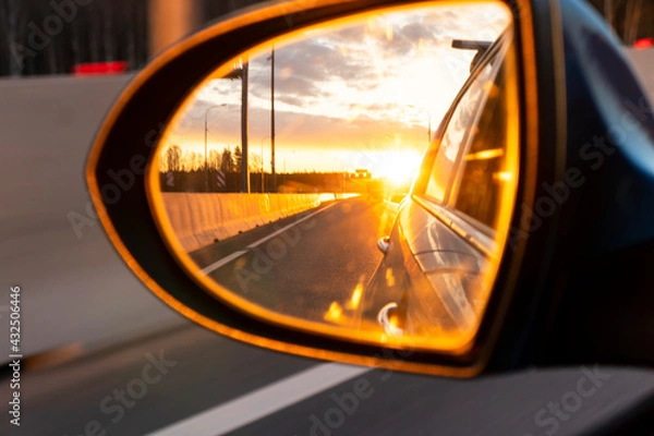 Fototapeta Rear view car mirror view back to nature on evening with sunset. Sunset reflected in the mirror of the car road car and landscape