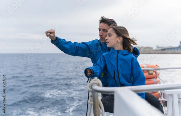 Fototapeta Father gesticulating while teaching to his son as they sail a boat at sea.