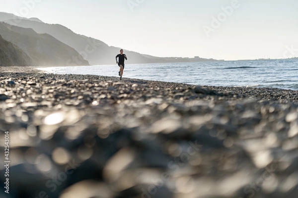 Fototapeta Man run on the beach, mountains background