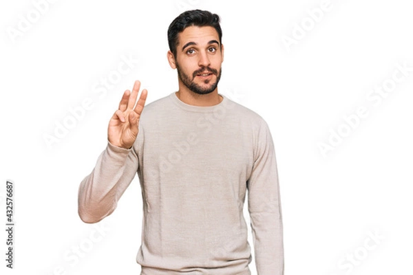 Fototapeta Young hispanic man wearing casual clothes showing and pointing up with fingers number three while smiling confident and happy.