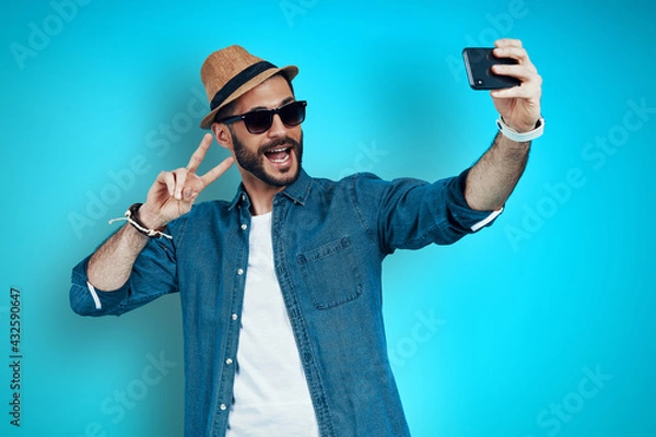 Fototapeta Playful young man smiling and taking selfie 