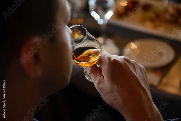 Obraz Man holding glass of cognac close to nose smelling the aroma